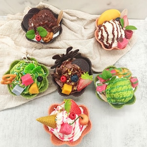 Puede incluir: Una colección de postres de helado decorativos y coloridos. Cada postre está en un cuenco de gofre y cubierto con varias frutas, salsas y aderezos. Los helados incluyen sabores de chocolate, mango y sandía, con elementos decorativos como hojas de menta.