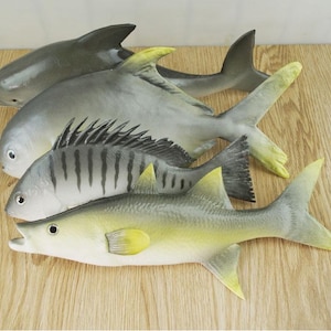 May include: Four realistic-looking fish toys, including a grey dolphin, a grey and white fish with black stripes, and two grey and yellow fish. The fish are made of a soft, pliable material and are perfect for imaginative play.