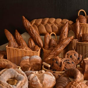 Op de afbeelding: Een selectie van bruine broden in rieten manden. Het brood is in een stilleven-compositie gerangschikt, met sommige broden in manden en andere los.