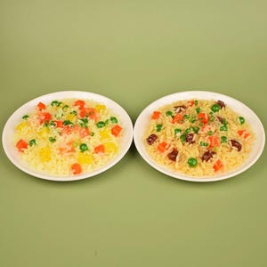 Puede incluir: Dos platos blancos de arroz con verduras coloridas. Un plato tiene verduras amarillas, naranjas y verdes en cubitos. El otro plato tiene verduras naranjas, verdes y marrones en cubitos. Los platos están sobre un fondo verde.