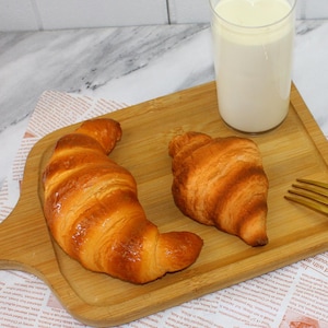 Op de afbeelding: Twee goudbruine croissants op een houten snijplank met een glas melk.
