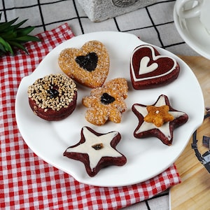 Puede incluir: Un plato blanco con seis galletas diferentes. Las galletas tienen forma de corazón, estrella, árbol y rosquilla. Las galletas están decoradas con chispas, glaseado y chocolate.