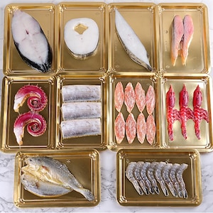 May include: A variety of fresh seafood presented in individual gold trays. The image shows fish fillets, octopus tentacles, shrimp, and other seafood, arranged on a marble-effect surface.