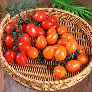 Puede incluir: Una cesta de mimbre llena de dos racimos de tomates cherry. Un racimo es rojo y el otro es naranja.