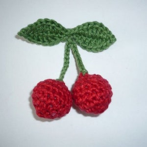 Könnte beinhalten: Zwei rote gehäkelte Kirschen mit grünen gehäkelten Blättern.