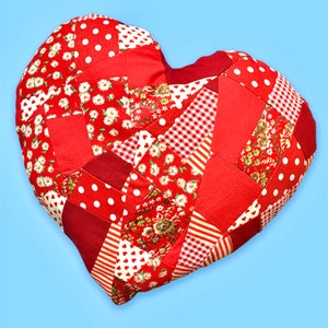 Könnte beinhalten: Ein rotes herzförmiges Kissen aus Patchworkstoff mit verschiedenen roten und weißen Mustern, darunter Punkte, Gingham und Blumenmuster.