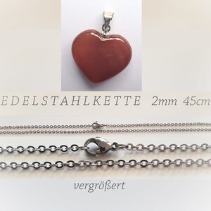May include: A red heart-shaped pendant with a silver chain. The chain is 45 cm long and 2 mm wide. The text "EDELSTAHLKETTE 2mm 45cm" is visible below the pendant. The chain is shown in two views, one with the clasp closed and one with the clasp open.