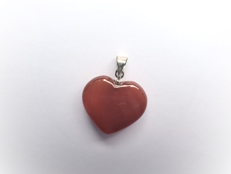 May include: A heart-shaped pendant made of carnelian, a reddish-orange gemstone, with a silver bail.