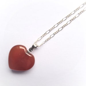 May include: A silver chain necklace with a heart-shaped carnelian pendant. The pendant is a deep reddish-orange color.
