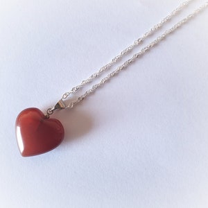 May include: A silver chain necklace with a red heart-shaped pendant.