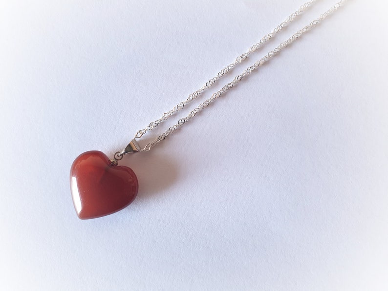 May include: A silver chain necklace with a red heart-shaped pendant.