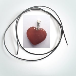 May include: A red heart-shaped pendant with a silver bail, hanging on a black leather cord.
