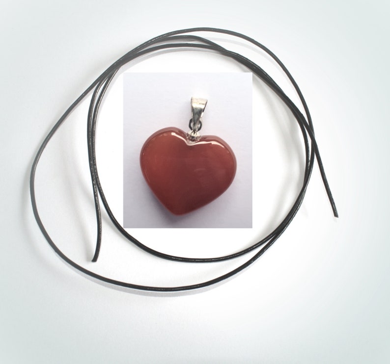 May include: A red heart-shaped pendant with a silver bail, hanging on a black leather cord.