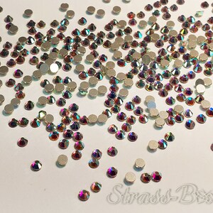 May include: A large quantity of iridescent rainbow-coloured rhinestones scattered on a white surface. The rhinestones are small and have a faceted design.