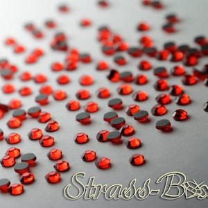 Peut inclure: Une dispersion de petits strass ronds rouges sur une surface blanche. Les strass ont un dos plat et une surface facetée brillante.