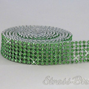 Peut inclure: Un rouleau de galon de strass vert avec des montures argentées. Le galon est enroulé et les strass sont tournés vers l'extérieur.