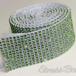 May include: A roll of green rhinestone trim with a silver backing. The trim is made of small, round rhinestones that are closely spaced together.
