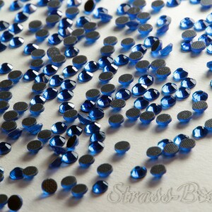 Könnte beinhalten: Eine Streuung kleiner, runder, blauer Strasssteine mit Kleberückseiten. Die Strasssteine befinden sich auf einer weißen Oberfläche.