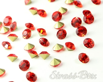 Op de afbeelding: Een strooiing van rode strass steentjes met gouden settings op een witte achtergrond. De strass steentjes zijn rond en hebben een facetgeslepen ontwerp.