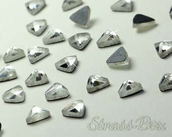 Puede incluir: Primer plano de un grupo de piedras de cristal de color plateado en forma de triángulo. Las piedras de cristal están esparcidas sobre una superficie blanca.