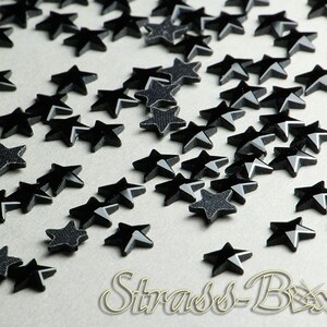 Peut inclure: Une dispersion de strass noirs en forme d'étoile sur une surface gris clair.