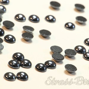 May include: A scattering of black, round, flat-backed rhinestones. The rhinestones have a shiny, reflective surface.