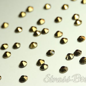 May include: A scattering of gold-toned rhinestones on a white surface. The rhinestones are small and have a faceted design.