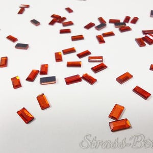 Puede incluir: Una dispersión de pequeños diamantes de imitación rectangulares de color naranja sobre una superficie blanca.