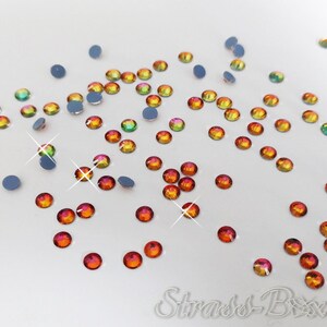 May include: A scattering of small, round, iridescent rhinestones in shades of orange, red, and green. The rhinestones are scattered on a white surface.