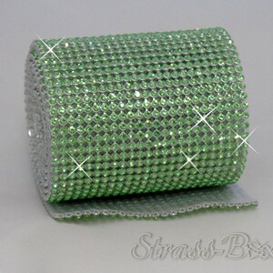 May include: A roll of green rhinestone ribbon. The ribbon is made of small, round rhinestones that are set in a mesh backing. The ribbon is rolled up and is ready to be used for crafting or decorating.