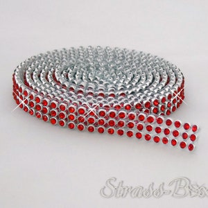 Puede incluir: Un rollo de ribete plateado con diamantes de imitación rojos. El ribete está enrollado y los diamantes de imitación están dispuestos en filas.