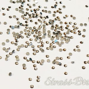 May include: A scattering of silver-toned rhinestones on a white background. The rhinestones are small and round, with a flat back and a faceted front.