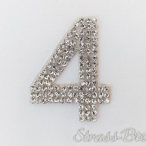 May include: A silver rhinestone number four iron-on patch. The number is made of clear rhinestones on a clear adhesive backing.