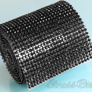 May include: A roll of black rhinestone trim. The trim is made of small, round rhinestones that are closely spaced together. The trim is rolled up and is ready to be used for crafting or decorating.