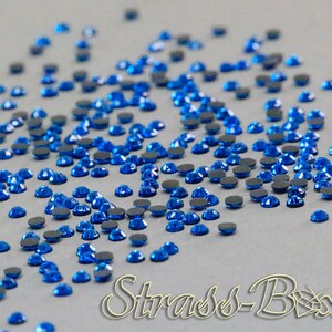 May include: A scattering of small, round, blue rhinestones with a silver backing. The rhinestones are scattered on a light gray surface.