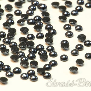 May include: A scattering of black pearl-like round beads with a flat back. The beads have a metallic sheen.