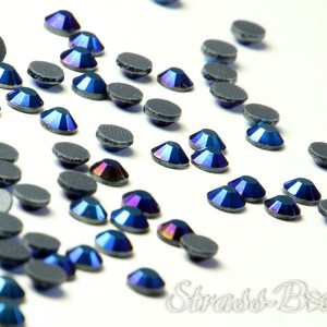 May include: A scattering of iridescent blue rhinestones with a black backing. The rhinestones are scattered on a white surface.