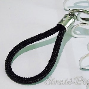 Pode incluir: Chaveiro de contas pretas com um anel prateado e um fecho prateado com um pequeno strass transparente.