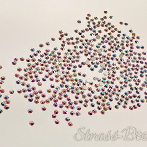 May include: A collection of iridescent rhinestones with a flat back, showing a range of colours such as pink, purple, and gold. These small, round rhinestones are suitable for crafts. The text "Strass-Bxx" is visible.
