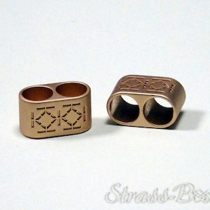 May include: Two bronze-colored metal beads with two holes each. The beads have a rectangular shape with decorative geometric patterns etched into the surface. The beads are displayed on a white background.