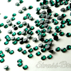 Può includere: Una spolverata di strass verde smeraldo su uno sfondo bianco. Gli strass sono di diverse dimensioni e forme, alcuni hanno un retro piatto e altri un retro appuntito.