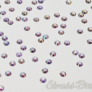 Peut inclure: Une dispersion de strass irisés sur un fond blanc. Les strass sont petits et ronds, avec une variété de couleurs, y compris le violet, le bleu et le vert.