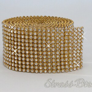 Puede incluir: Un rollo de ribete de strass de color dorado con strass transparentes. El ribete está hecho de pequeños strass redondos que están engastados en un engaste de metal dorado.
