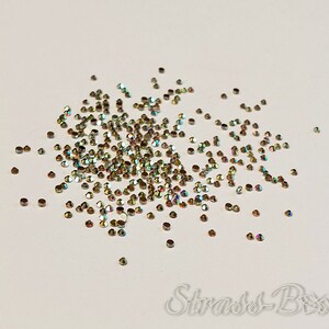 May include: A scattering of iridescent gold rhinestones on a white background. The rhinestones are small and round, with a slight sparkle.