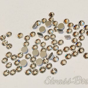 May include: A scattering of clear glass rhinestones, some with silver backing, on a white surface.  The rhinestones are various sizes and shapes.