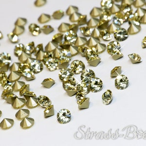 Pode incluir: Uma dispersão de pequenos strass transparentes e facetados com um tom dourado claro. Os strass têm um verso pontiagudo, o que os torna ideais para artesanato e embelezamento de projetos.
