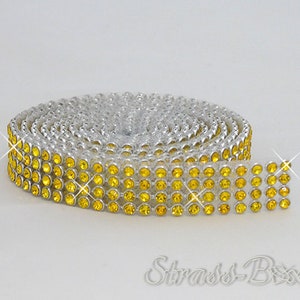 Peut inclure: Un rouleau de galon de strass jaune avec un dos argenté. Le galon est composé de petits strass ronds, serrés les uns contre les autres.
