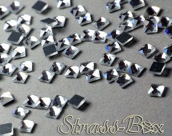 Puede incluir: Una dispersión de piedras de cristal cuadradas transparentes y facetadas sobre una superficie gris. Las piedras de cristal tienen un acabado reflectante, como un espejo.