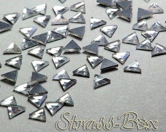 Puede incluir: Una dispersión de piedras de cristal triangulares transparentes y facetadas sobre un fondo gris. Las piedras de cristal están dispuestas en un patrón aleatorio y son de varios tamaños.