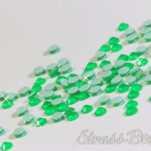 Può includere: Una grande quantità di piccoli strass rotondi verdi con retro adesivo. Gli strass sono sparsi su una superficie bianca.
